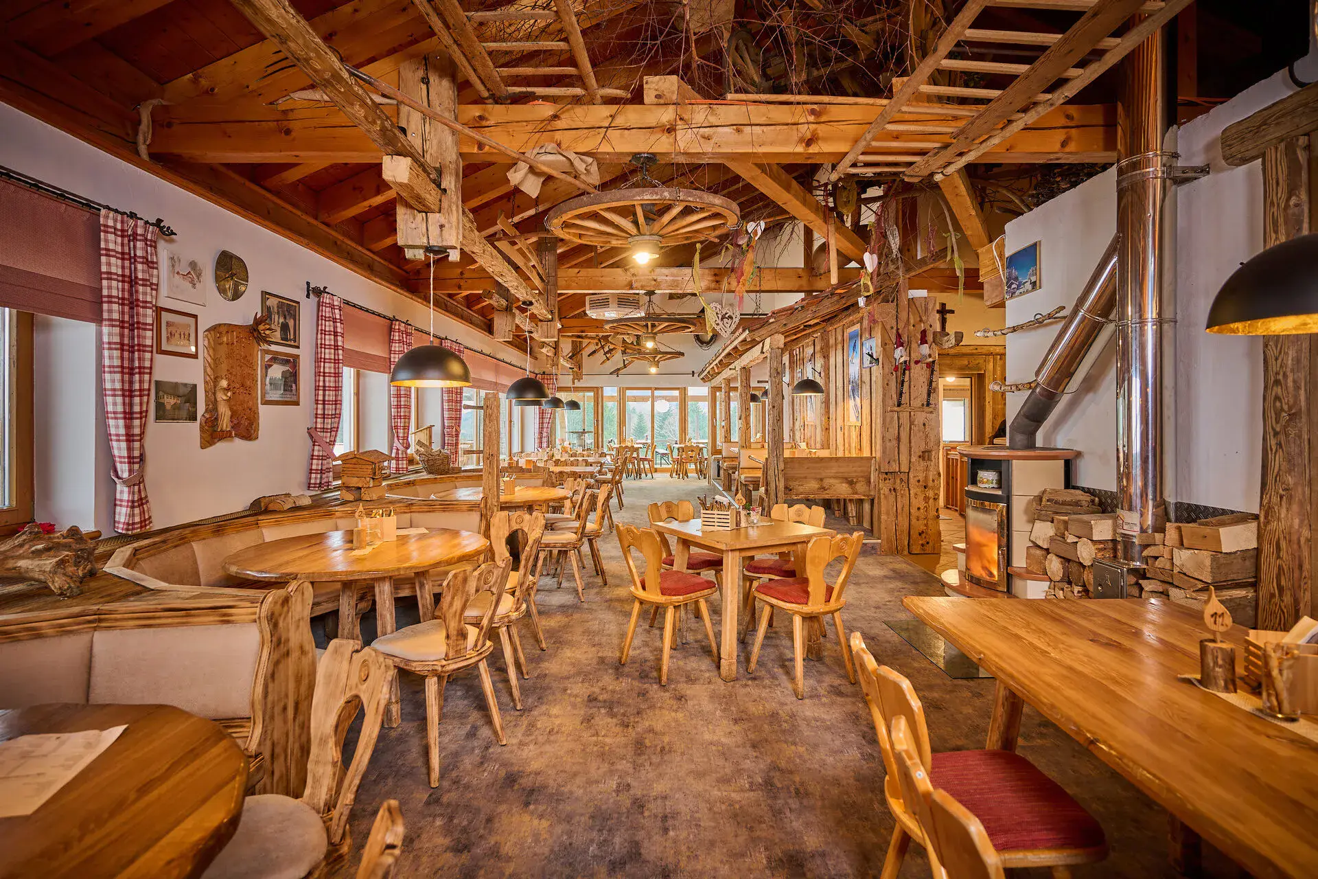 Gaststube der Stoaberg Alm am Steinberglift mit Holztischen, Wagenrad-Leuchter und Kachelofen