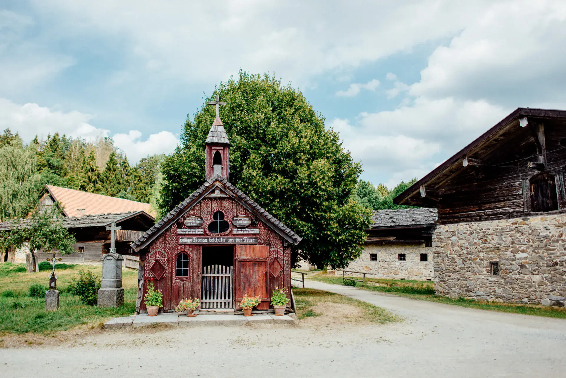Kleine rote Holzkapelle zwischen alten Bauernhäusern im Museumsdorf