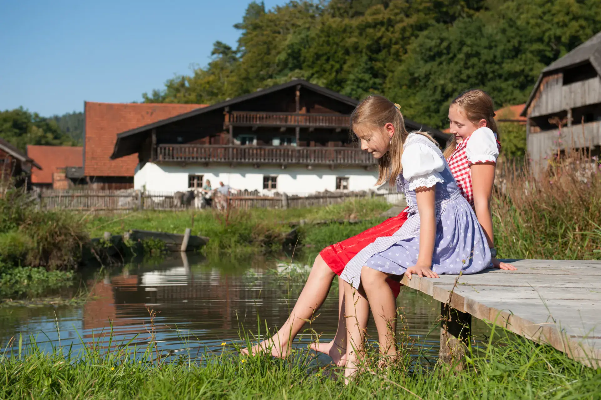Zwei Mädchen im Dirndl auf einem Holzsteg am Wasser im Museumsdorf