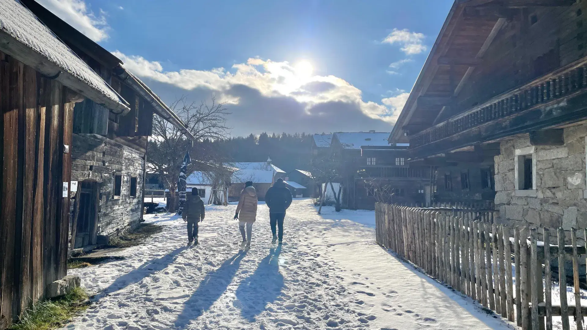 Besucher auf verschneitem Weg zwischen Holzhäusern im Museumsdorf im Winter