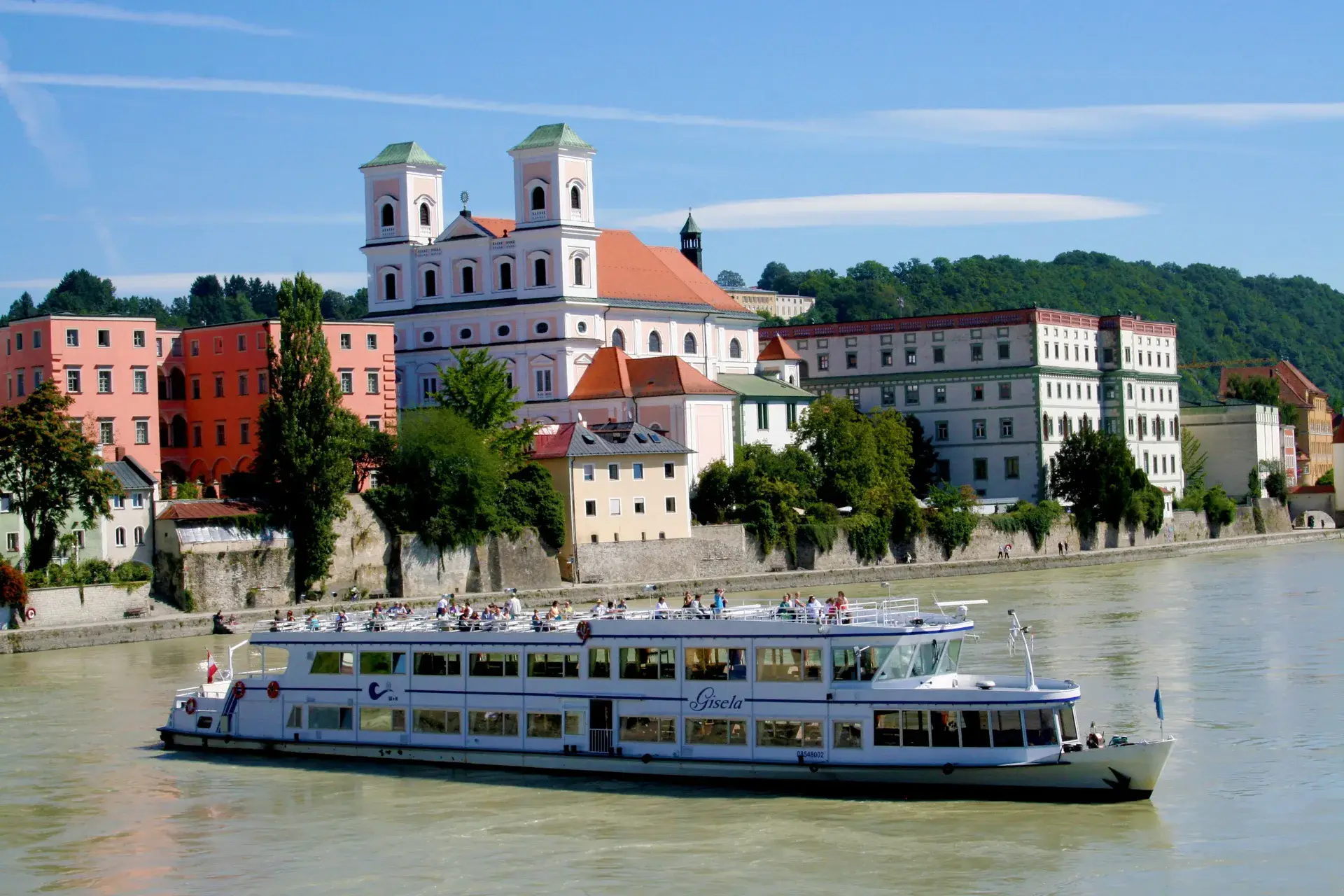 Ausflugsschiff auf dem Fluss vor der Passauer Altstadt mit einer weißen Kirche mit zwei Türmen