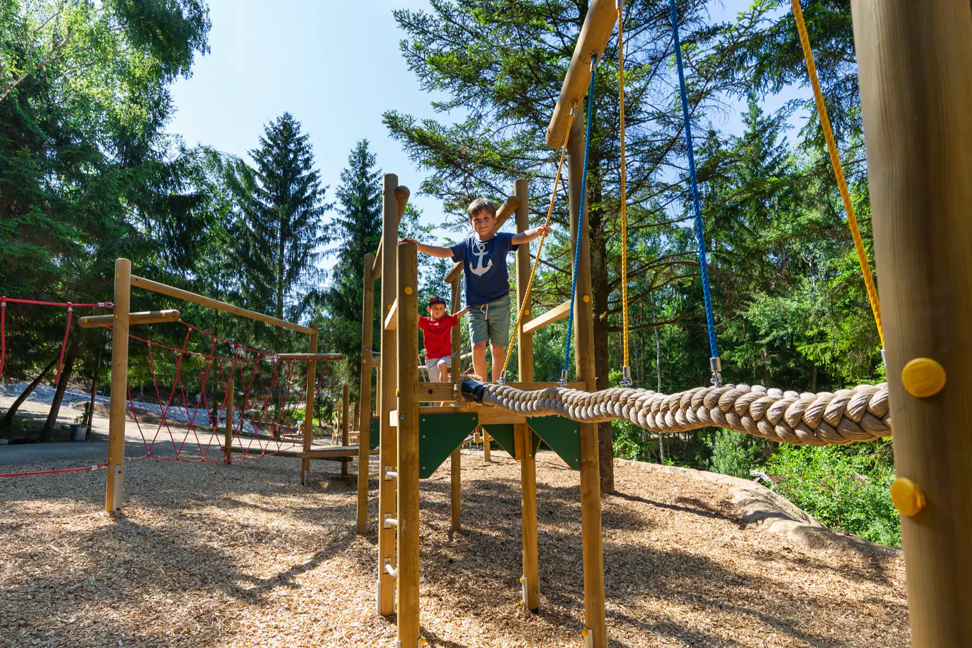 Kinder klettern auf dem Holzspielplatz zwischen Nadelbäumen in Pullman City