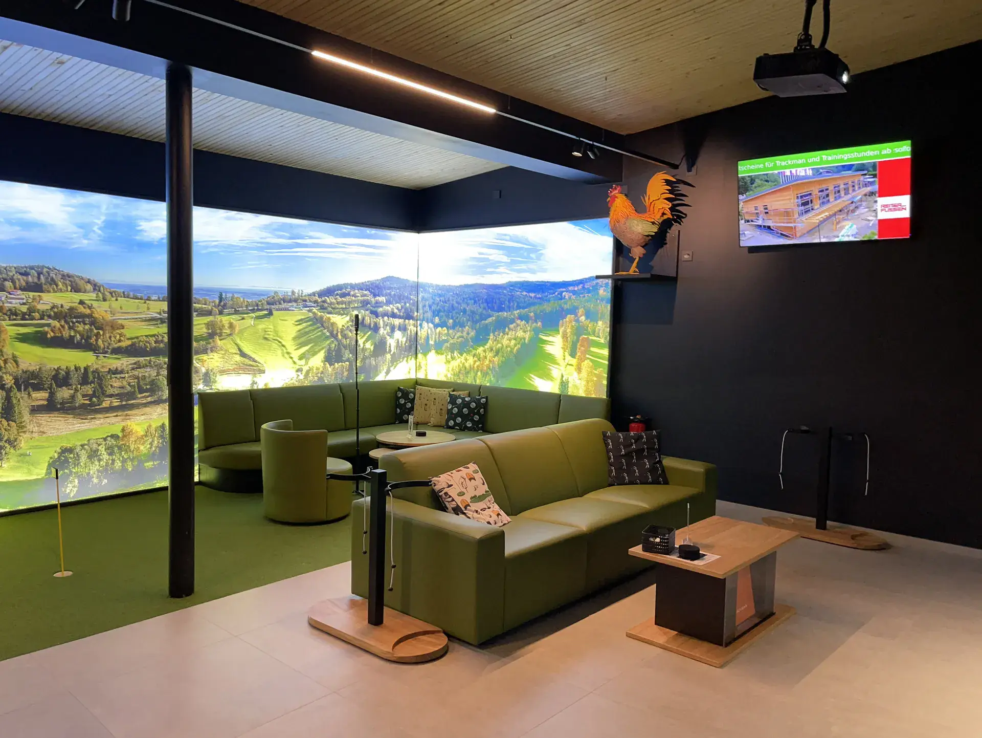 Lounge mit grünen Sofas vor einer Panorama-Simulatorleinwand mit Landschaftsbild in der Rusel-Arena