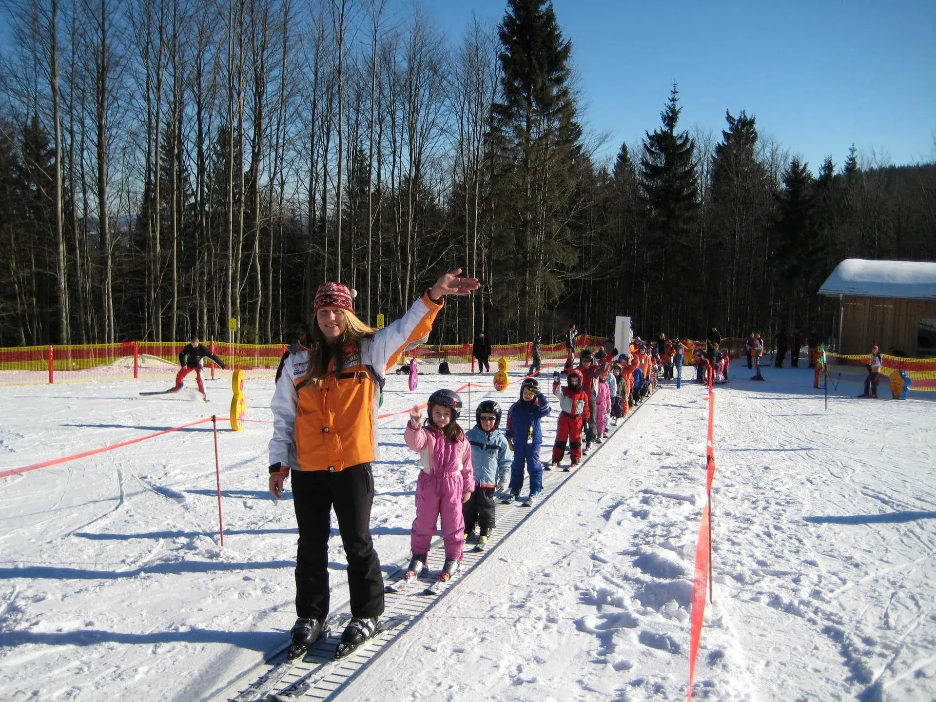 Skikurs im Kinderland am Steinberglift: Skilehrerin mit einer Reihe Kinder auf dem Förderband